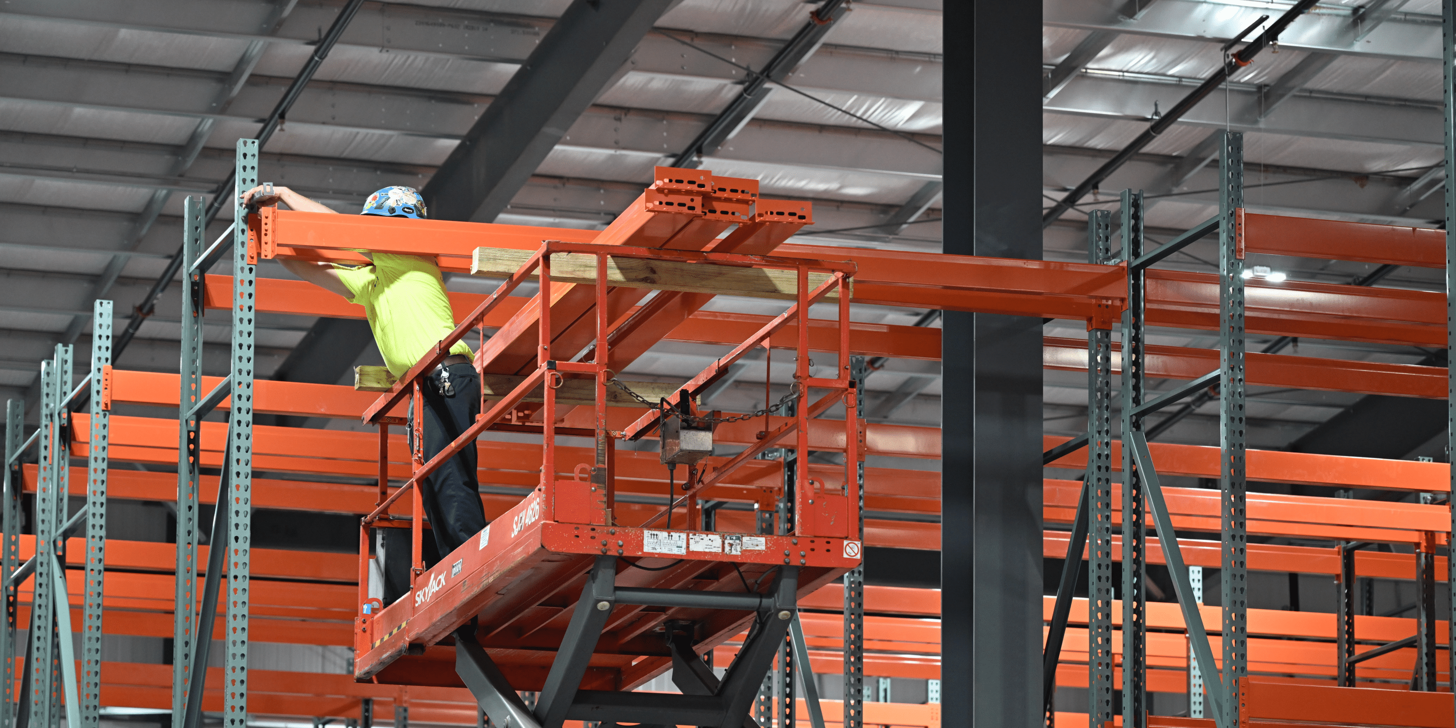 Skyjack equipment example showing employee on heightened scissor lift leaning over to drill something